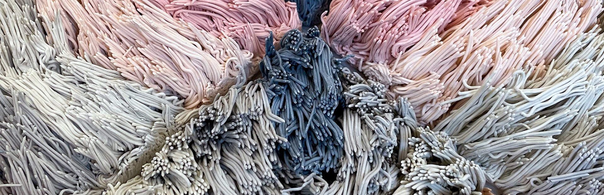 Detail photo of a pink and blue ceramic sculpture of a geometric patterned shag rug by Risa Hricovsky.