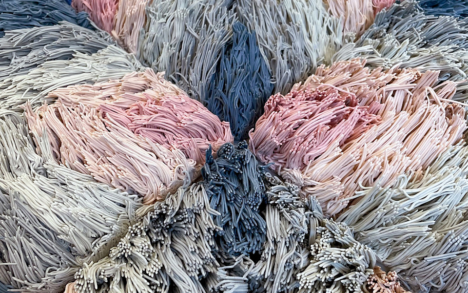 Detail photo of a pink and blue ceramic sculpture of a geometric patterned shag rug by Risa Hricovsky.