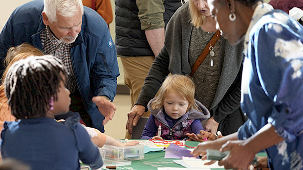 Photo of small children, parents, and grandparents gathered around a table doing crafts.