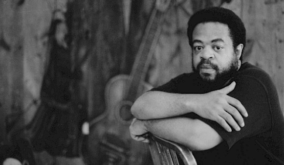 Black and white photo of Whitfield Lovell sitting in a chair in his studio.