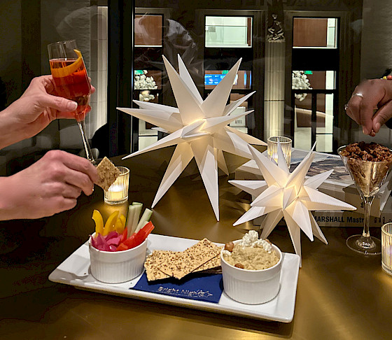 Photo of two sets of hands holding cocktails and reaching for snacks on a table decorated with votive candles and paper stars.