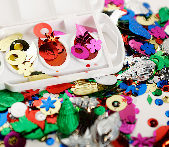 Photo of a variety of sequins in different shapes and colors on a white tabletop.