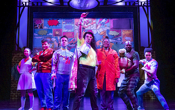 Photo of the cast of An Unlikely Hero posed together on stage in superhero stances.