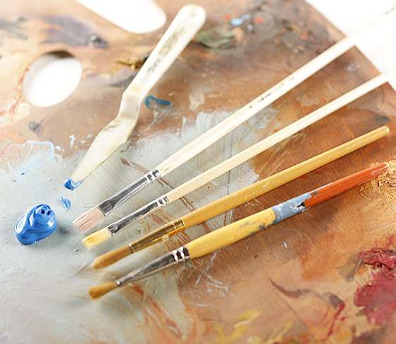 Photo of several paintbrushes and a dollop of blue paint laying on an artist palette.