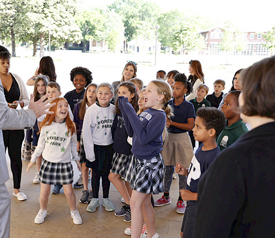 Photo of school children wearing uniforms and smiling in reaction to an animated tour guide.