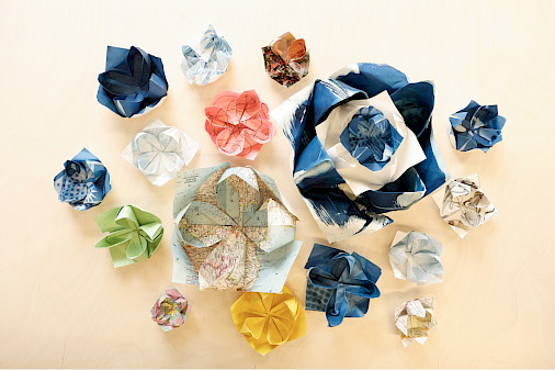 Photo of origami lotuses of various sizes and colors sitting on a light wooden table.