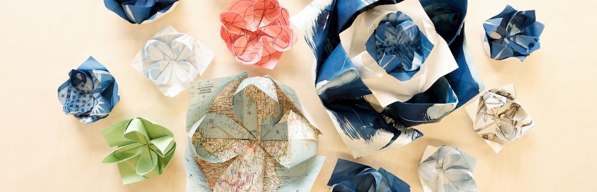 Photo of origami lotuses of various sizes and colors sitting on a light wooden table.