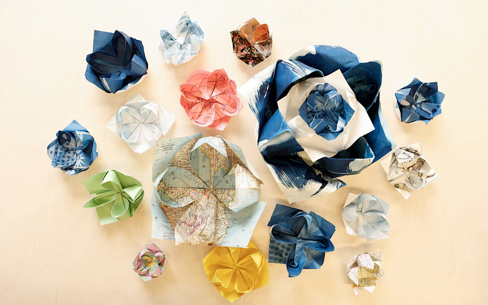 Photo of origami lotuses of various sizes and colors sitting on a light wooden table.