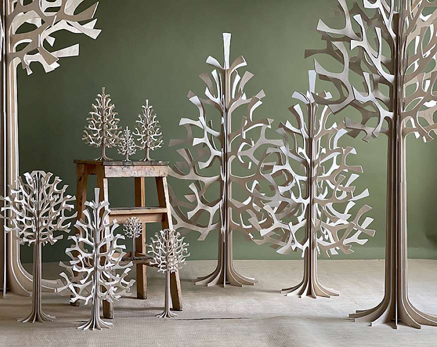 Photo of several cut paper trees of various sizes in a room with a dark green wall.