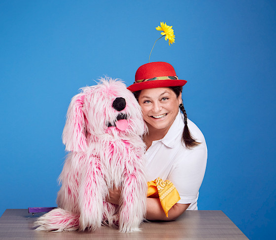 Photo of a pink puppet dog and a puppeteer.